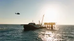 Hubschrauber fliegt nahe einer Ölplattform und einem Schiff