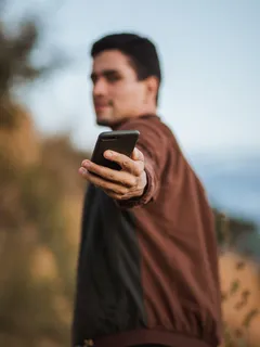 Mann in braunem Hemd hält schwarzes Smartphone in der Hand